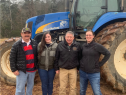 Sarah standing with farmers in front of a blue tractor